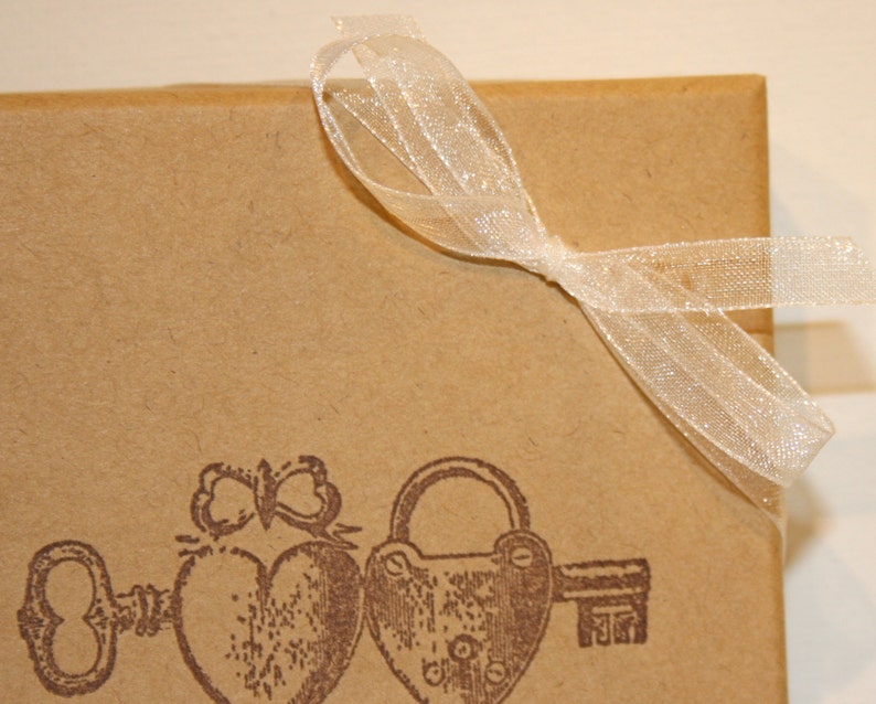 May include: A brown paper gift box with a white ribbon tied in a bow. The box features a vintage design with a key, a heart, and a padlock printed on the front.