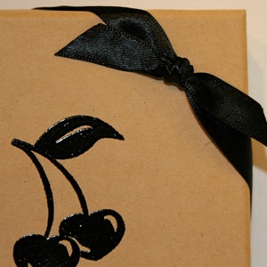 Peut inclure: Un sac cadeau en papier brun avec un ruban de satin noir nou&eacute; en un n&oelig;ud. Le sac a une silhouette noire de deux cerises avec une tige et une feuille.