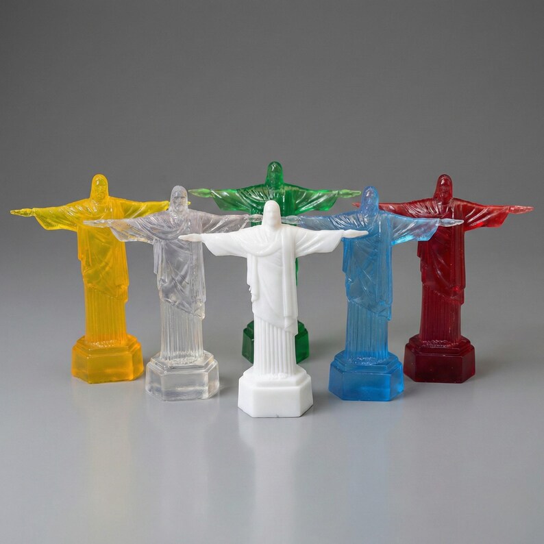 May include: A collection of miniature statues of Christ the Redeemer in various colors, including yellow, clear, green, white, blue, and red. Each statue has outstretched arms and stands on a rectangular base. The statues are made of a translucent material.