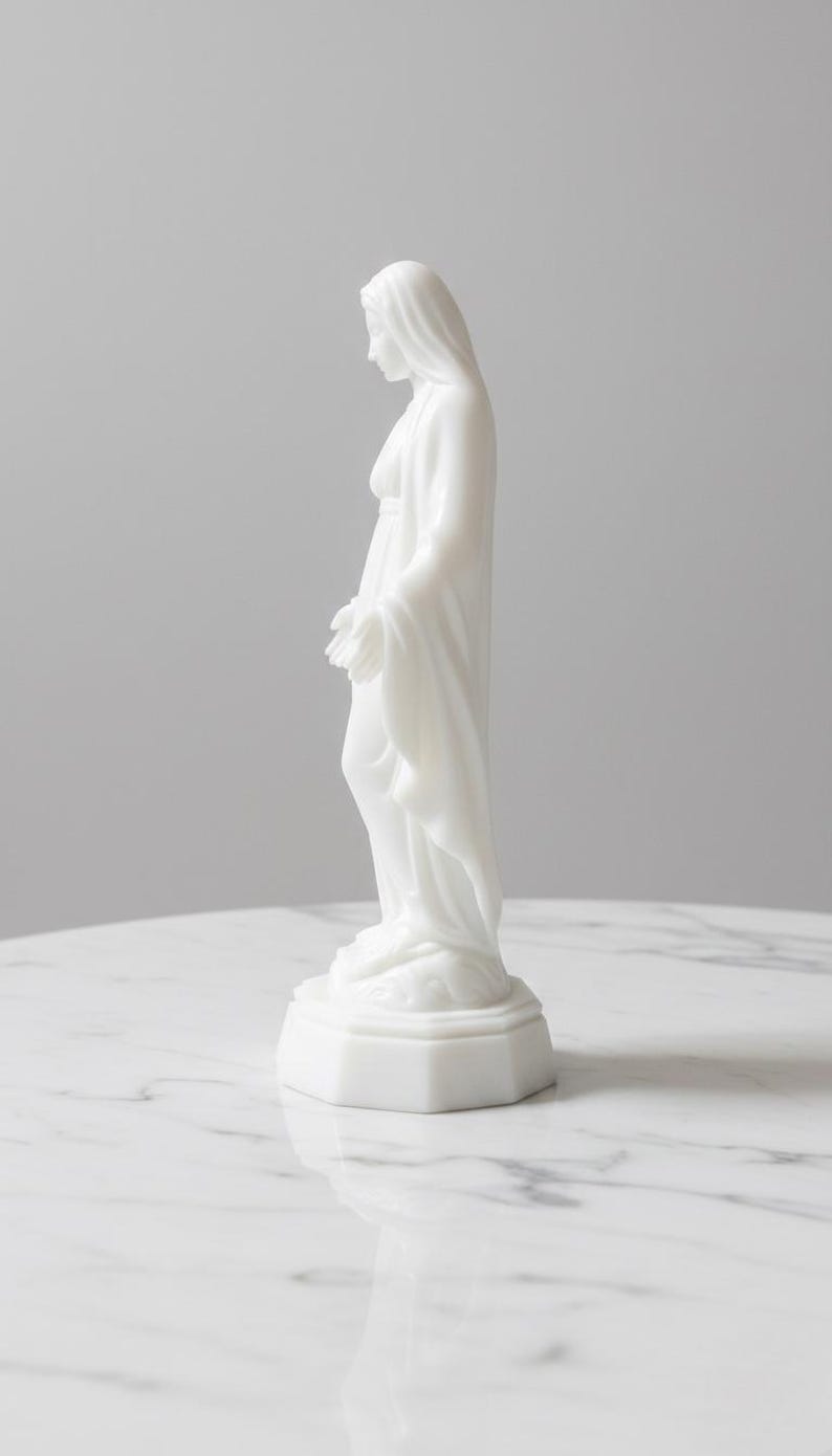 May include: A white, opaque, smooth-surfaced figurine of a standing figure with a draped head covering and long robes. The figure is positioned in profile, facing downward with hands slightly extended, resting on a hexagonal base.