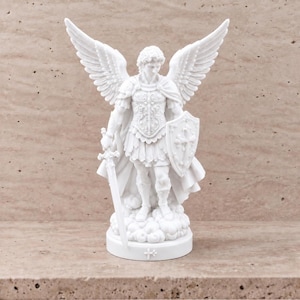 May include: A white statue of an archangel with large wings, wearing detailed armor and a flowing cape. The figure holds a sword in the right hand and a shield with a cross emblem in the left, standing atop a cloud base on a circular plinth.