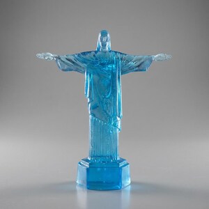 May include: A translucent blue statue of Christ the Redeemer with outstretched arms. The statue is mounted on a hexagonal base. The sculpture is a detailed replica of the iconic landmark.