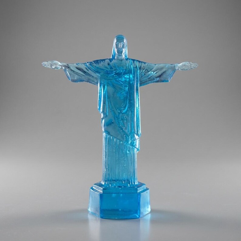 May include: A translucent blue statue of Christ the Redeemer with outstretched arms. The statue is mounted on a hexagonal base. The sculpture is a detailed replica of the iconic landmark.
