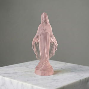 May include: A translucent pale pink glass figurine depicting a standing figure with arms outstretched, wearing a long, flowing robe with pleated details. The figure is positioned on a hexagonal base and features a smooth, frosted finish throughout.