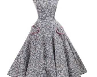 May include: A vintage-style dress with a gray and pink speckled pattern. The sleeveless dress features a scoop neckline and two front pockets, both trimmed with pink. The dress has a full skirt and is displayed on a mannequin.