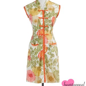 May include: A vintage floral print dress with a mandarin collar and orange trim. The sleeveless dress features a white background with large pink, yellow, and orange roses and green leaves. The dress has orange frog closures and two small pockets.