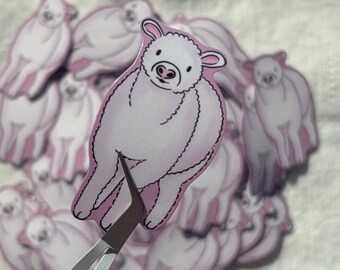 May include: A collection of white and pink stickers featuring a cartoon lamb design. The stickers are held by a pair of silver tweezers with the word "Cricut" printed on the side. The stickers are on a white fabric background.