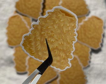 May include: A collection of stickers featuring a detailed illustration of a golden, textured object, possibly food. The stickers are held by tweezers, with several others arranged in the background. The stickers have a white border.