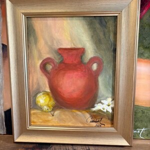 Puede incluir: Pintura enmarcada de naturaleza muerta con un jarrón rojo con asas, una fruta amarilla y flores blancas. La obra está firmada y fechada, sobre un fondo apagado con un marco dorado.