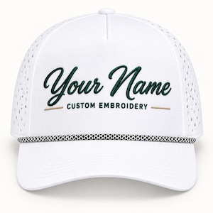 May include: A white baseball cap featuring a perforated side panel design and a black and white braided cord across the base of the crown. The front displays the dark green embroidered text Your Name and the words CUSTOM EMBROIDERY in black.