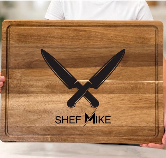 A wood cutting board shaped and engraved around a BBQ/grill master theme — the specific niche angle and detailed grill imagery make it a notch above a plain name board.