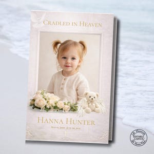 May include: A memorial card with a photograph of a young child. The card includes the text "Cradled in Heaven" and the name "Hanna Hunter" with dates. A teddy bear with angel wings and flowers are also featured. The card is in soft, neutral tones.