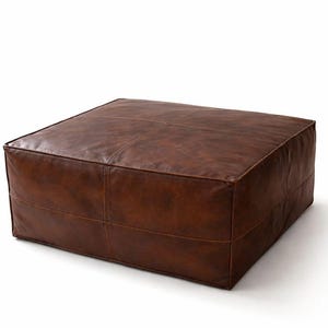 Könnte beinhalten: Ein quadratischer, brauner Lederhocker mit Steppnähten. Der Hocker hat einen satten, warmen Braunton und scheint aus hochwertigem Leder gefertigt zu sein. Er hat eine niedrige, quadratische Form und eignet sich als Fußstütze oder zusätzliche Sitzgelegenheit.