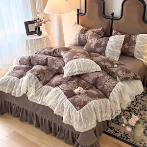 May include: A bed with a brown floral patterned comforter and matching pillows. The comforter and pillowcases have white lace trim. The bed has a brown bed skirt and a dark brown headboard. The room has a soft, romantic feel.