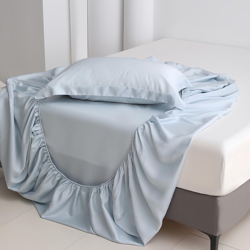 Puede incluir: Un juego de s&aacute;banas azul claro sobre una cama. El juego incluye una s&aacute;bana bajera, una s&aacute;bana encimera y una funda de almohada. Las s&aacute;banas est&aacute;n hechas de un material suave y sedoso. El marco de la cama es gris.