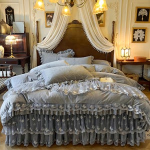 May include: A grey bedding set featuring a duvet cover and pillow shams with ruffled edges. The fabric is adorned with a delicate white butterfly pattern and lace trim. The set includes a layered bed skirt with matching butterfly embroidery.