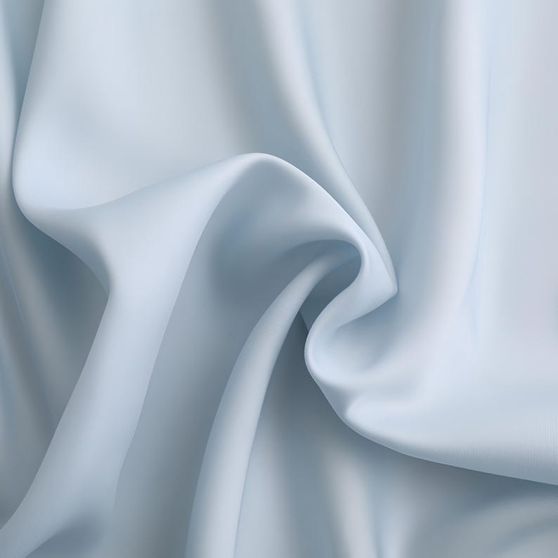 Puede incluir: Primer plano de una tela azul claro con pliegues suaves y una textura fluida. La tela parece lisa y tiene un brillo sutil, creando una sensaci&oacute;n de movimiento y profundidad. El color es un tono azul p&aacute;lido y calmante.
