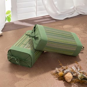 May include: Two rectangular green and beige striped pillows with green trim and end caps. The pillows are made of woven material and have a decorative bow on each end. The pillows are placed on a patterned surface.