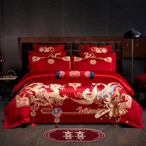 Peut inclure: Une parure de lit rouge ornée de motifs brodés dorés représentant un dragon et un phénix, comprenant une housse de couette, quatre taies d'oreiller et un traversin cylindrique. Un tapis ovale assorti porte le symbole du double bonheur et le texte LOVE.