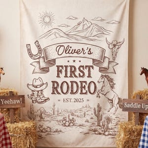 May include: A beige fabric backdrop with a brown illustration of a rodeo scene. The text "Oliver's First Rodeo" is displayed, along with a horseshoe, cowboy boots, a horse, and cacti. The year "EST. 2025" is also included.
