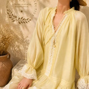 May include: A pale yellow long-sleeved dress featuring a ruffled collar, white lace trim along the front placket, cuffs, and hem, and a straw hat. The text "BOHEME SOCIETY COLLECTIVE CURATED BOHEMIAN WOMENSWEAR" is printed in the upper left corner.