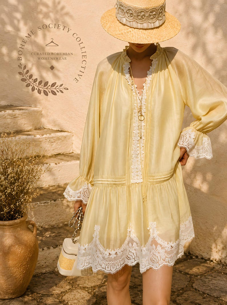May include: A pale yellow long-sleeve dress featuring white lace trim along the neckline, cuffs, and hem. The dress has a ruffled collar, a drop-waist silhouette, and a delicate fabric texture. A straw hat with a wide brim is worn above.