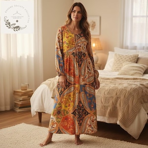 May include: A long, patterned maxi dress with a paisley design in shades of yellow, orange, blue, and black. The dress has long sleeves, a V-neck with a tie, and a patchwork style. The dress is floor-length and has a relaxed fit.