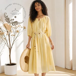 Yellow boho midi dress for women featuring lightweight Tencel fabric, romantic puff sleeves, flowing A-line silhouette, and adjustable lace-up waist detail. Feminine cottagecore summer dress with soft airy texture and relaxed fit perfect for brunch dates, vacations, garden parties, tea parties, casual chic styling, and everyday elegance. Pastoral-inspired midi dress in buttery yellow tone designed for breathable comfort and graceful movement during spring and summer wear.