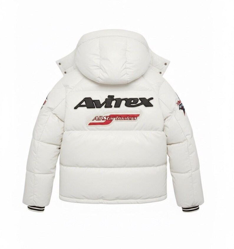 Puede incluir: Chaqueta acolchada blanca con capucha, con el nombre de la marca "Avirex" en letras negras y rojas en la espalda. La chaqueta tiene un dise&ntilde;o acolchado, pu&ntilde;os a rayas blancas y negras y parches en las mangas.