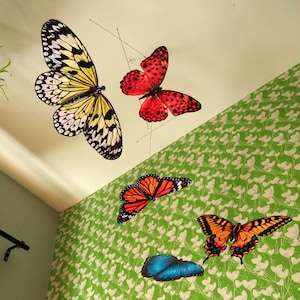 Puede incluir: Un móvil colgante con cinco adornos de mariposas suspendidos de hilos finos. Las mariposas incluyen una grande amarilla y negra, una roja con puntos negros, una monarca naranja y negra, una mariposa cola de golondrina y una mariposa azul sólida.