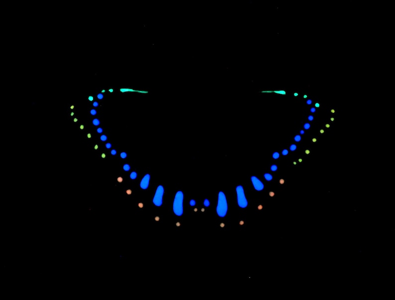 May include: A symmetrical arrangement of glowing dots and teardrop shapes against a solid black background. The pattern features a central row of bright blue teardrops, flanked by curved lines of smaller blue, light green, and soft orange dots.