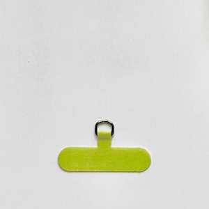 Op de afbeelding: Een limoengroen, rechthoekig zelfklevend lipje met afgeronde uiteinden, voorzien van een kleine, zilverkleurige metalen D-ring in het midden aan de bovenkant. Het oppervlak van het lipje heeft een fijne, getextureerde afwerking voor bevestiging.