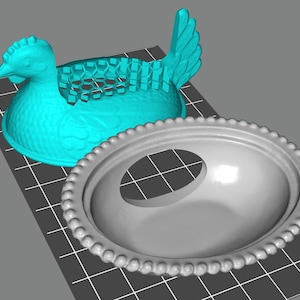 May include: A turquoise hen-shaped container with a honeycomb design on its back, paired with a gray oval dish. The dish has a decorative beaded edge and an egg-shaped opening. This item is likely for kitchen or home decor.