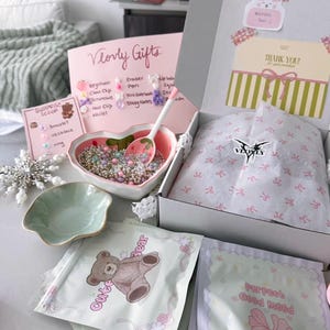 May include: A gift box with pink and white accents, containing a heart-shaped bowl filled with beads, a spoon, and various small accessories. Includes a card that says "Vlovly Gifts" and a "Thank You" card.