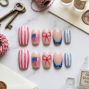 May include: A set of ten artificial nails with various designs. Some nails feature red and white stripes, while others display an American flag, a red bow, or blue and white stripes. The nails are arranged on a white surface.