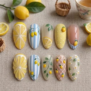 May include: A collection of ten almond-shaped nail designs with a lemon theme. The designs include 3D lemon slices, stripes, polka dots, and floral patterns. The color palette features yellow, white, blue, and brown hues. Lemons, lemon slices, and small baskets are arranged around the nails.