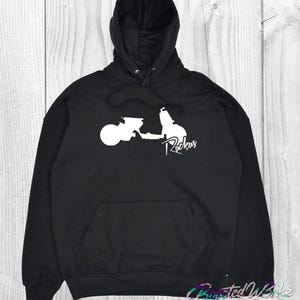 May include: Black hooded sweatshirt with a white scooter graphic and the word "Ruckus" in a stylized font. The sweatshirt has a front pocket and a drawstring hood. The bottom right corner of the image has the text "BustedWrkz EST. 2026".