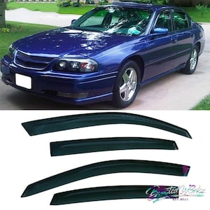May include: A blue sedan with tinted windows and a set of four dark-tinted window visors. The car is parked on a paved surface with green grass and trees in the background. The visors are black.