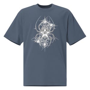 Op de afbeelding: Een leiblauw t-shirt met korte mouwen en een witte grafische print op de borst. Het ontwerp bestaat uit een centrale vijfpuntige ster met een dollarteken erin, omringd door ingewikkelde, stekelige, webachtige patronen en kleine cirkels.