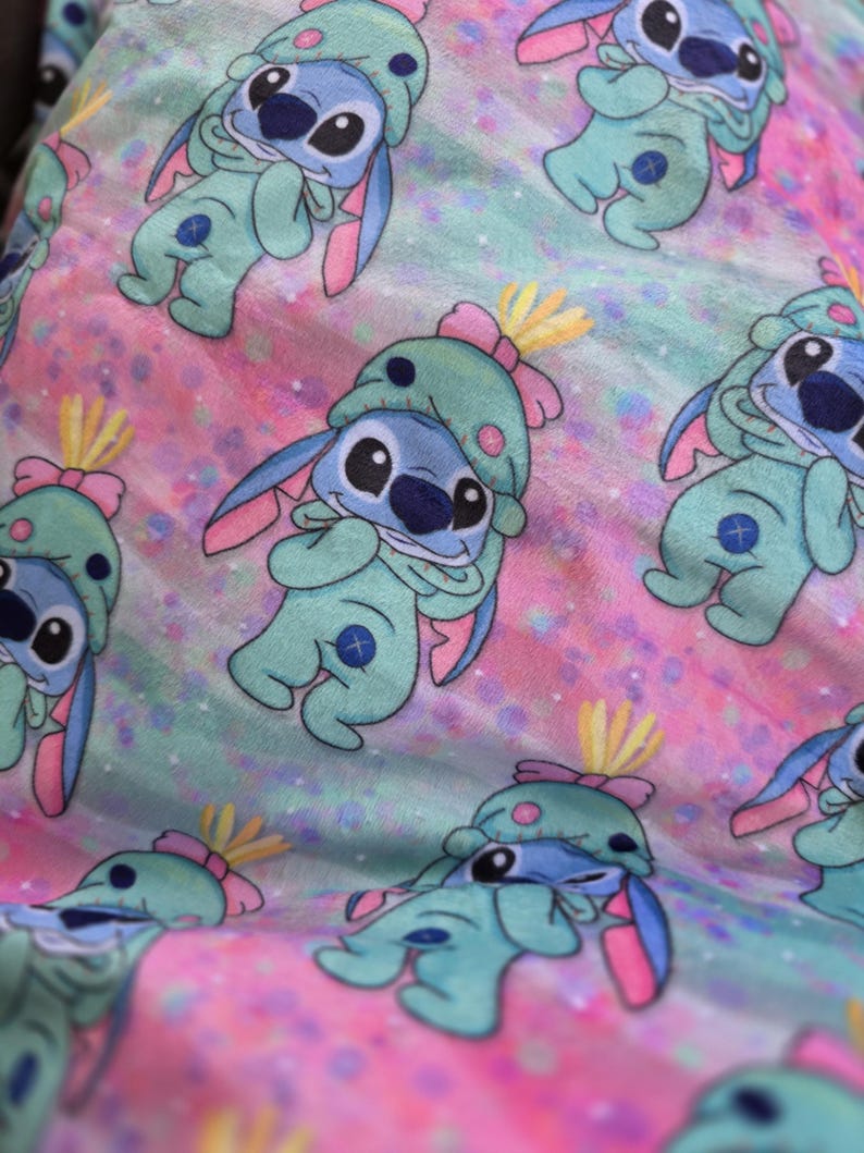 Puede incluir: Patr&oacute;n repetitivo del personaje Stitch de la pel&iacute;cula Lilo & Stitch. El personaje est&aacute; representado en un mono azul claro con un gorro a juego y detalles en rosa, sobre un fondo pastel rosa y azul.