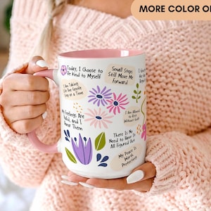May include: A white ceramic mug with a pink interior and handle, featuring colorful floral illustrations and inspirational text including phrases like Today, I Choose to Be Kind to Myself and My Peace Is Worth Protecting.