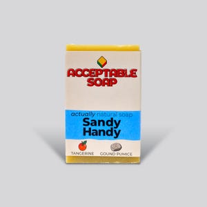 May include: A rectangular bar of "Acceptable Soap" with a label that reads "Sandy Handy" and "actually natural soap." The label also features a tangerine and a pumice stone illustration. The soap is yellow.