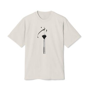 Op de afbeelding: Crèmekleurig T-shirt met een zwarte afbeelding van een toren en Arabische kalligrafie. Het shirt met korte mouwen heeft een ronde hals en een relaxte pasvorm, geschikt voor casual wear.