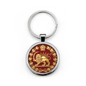 Puede incluir: Un llavero redondo con un anillo plateado y un colgante circular. El colgante presenta un león dorado sosteniendo una espada, una corona y rayos de sol sobre un fondo rojo, rodeado de hojas de laurel doradas.