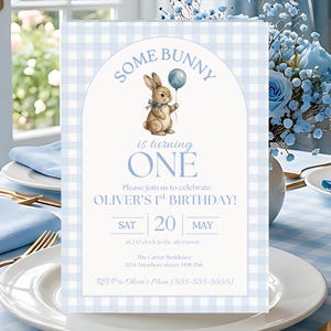 K&ouml;nnte beinhalten: Eine hellblaue und wei&szlig;e karierte Einladungskarte mit dem Text "SOME BUNNY is turning ONE". Die Karte zeigt eine Aquarellillustration eines Hasen mit einem Ballon. Die Einladung ist f&uuml;r Olivers 1. Geburtstag.