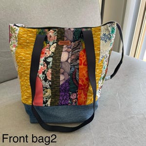 May include: A patchwork tote bag with a denim base and black straps. The bag features a variety of colourful fabric strips, including floral and geometric patterns. The text "Front bag2" is visible at the bottom.