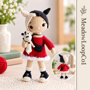 Puede incluir: Una muñeca de ganchillo hecha a mano con cabello dividido en negro y blanco, vistiendo un vestido rojo con borde blanco, zapatos negros y un pequeño bolso cruzado negro. La muñeca sostiene un peluche blanco con puntos negros. Texto MeadowLoopCol.