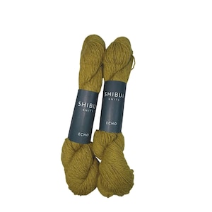 May include: Two skeins of Shibui Knits Echo yarn in a muted olive green color. Each skein has a dark teal label with the brand name and yarn type. The yarn is tightly wound and appears soft, ideal for knitting or crochet projects.