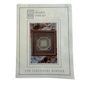 May include: A white paper pattern booklet titled The Drawn Thread Charted Needlework Designs The Perennial Border. The cover features a square framed embroidery piece with a floral border and a central geometric pattern on a brown background.