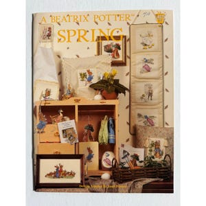 May include: A Beatrix Potter Spring craft pattern book cover featuring illustrations of Peter Rabbit and friends. The image displays various finished projects including framed cross-stitch, a hanging wall organizer, and a wooden cabinet.
